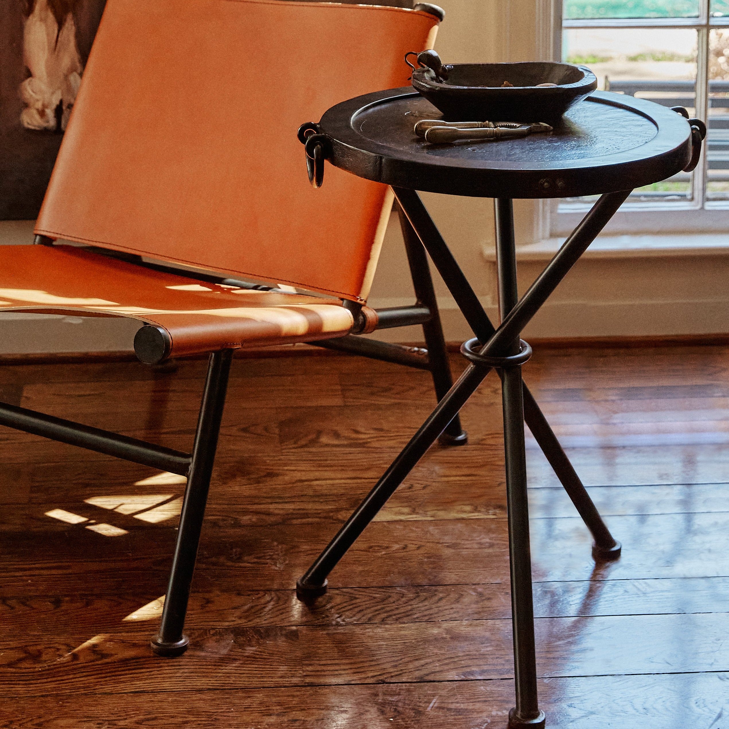 A brown chair next to a tripod  table with a bowl . On the background is a window.
