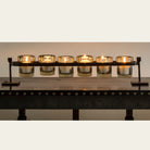 Lit candles inside a wax cast railroad with six mouth blown glass votive holders on forged stand