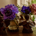 Two purple flowers and a rose in some glasses with iron coaster. Two iron angels in front.