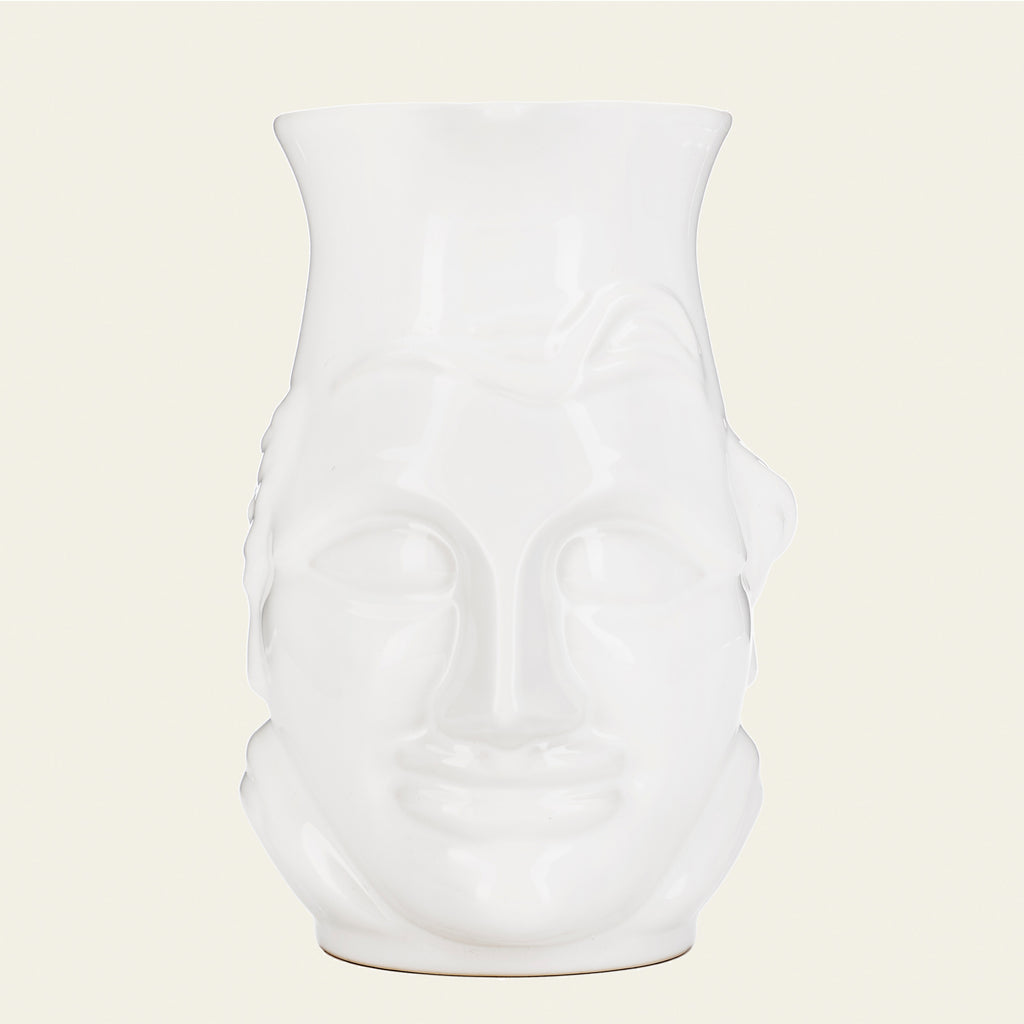 A white ceramic pitcher with a face. Light cream color background.