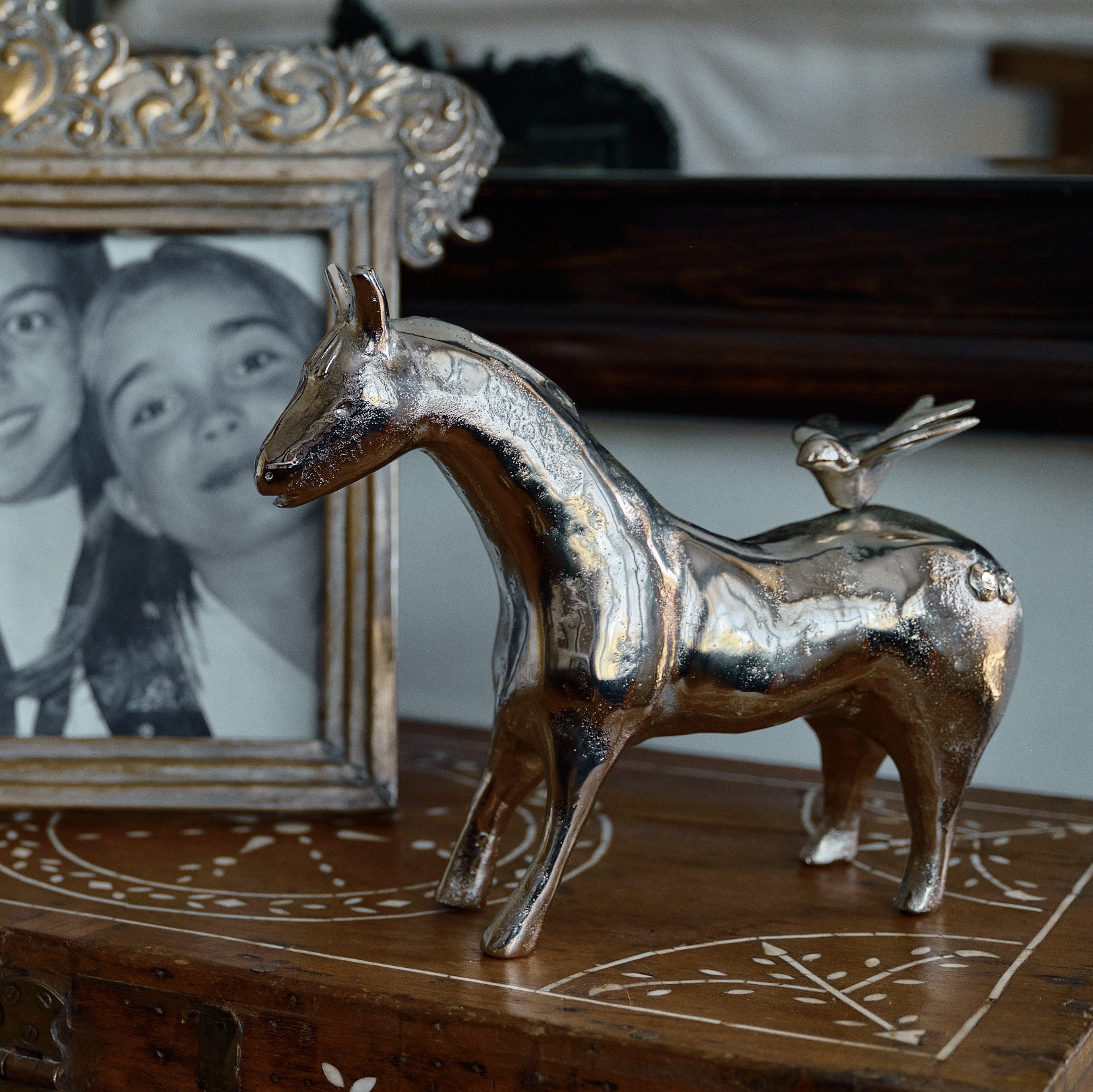 A nickel horse bank with a bird on its back. on top of a wood  surface next to a picture frame.