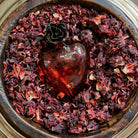 Mouth blown puffed red glass heart with a tiny iron rose on top of purple and pink dried leaves.
