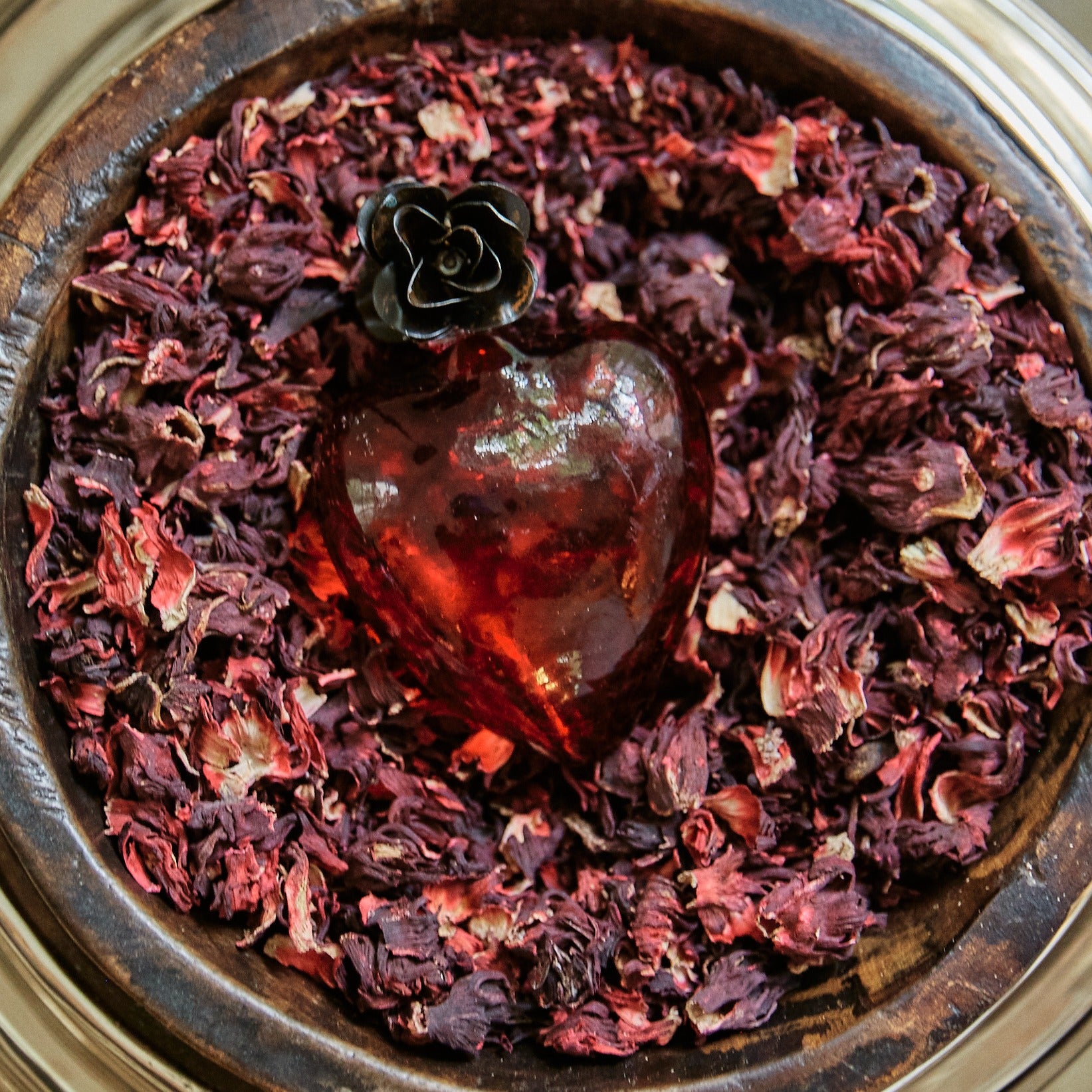 Mouth blown puffed red glass heart with a tiny iron rose on top of purple and pink dried leaves.