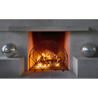 A gray wall with a lit chimney, an arched iron fire screen in front and to each side a grey ball.