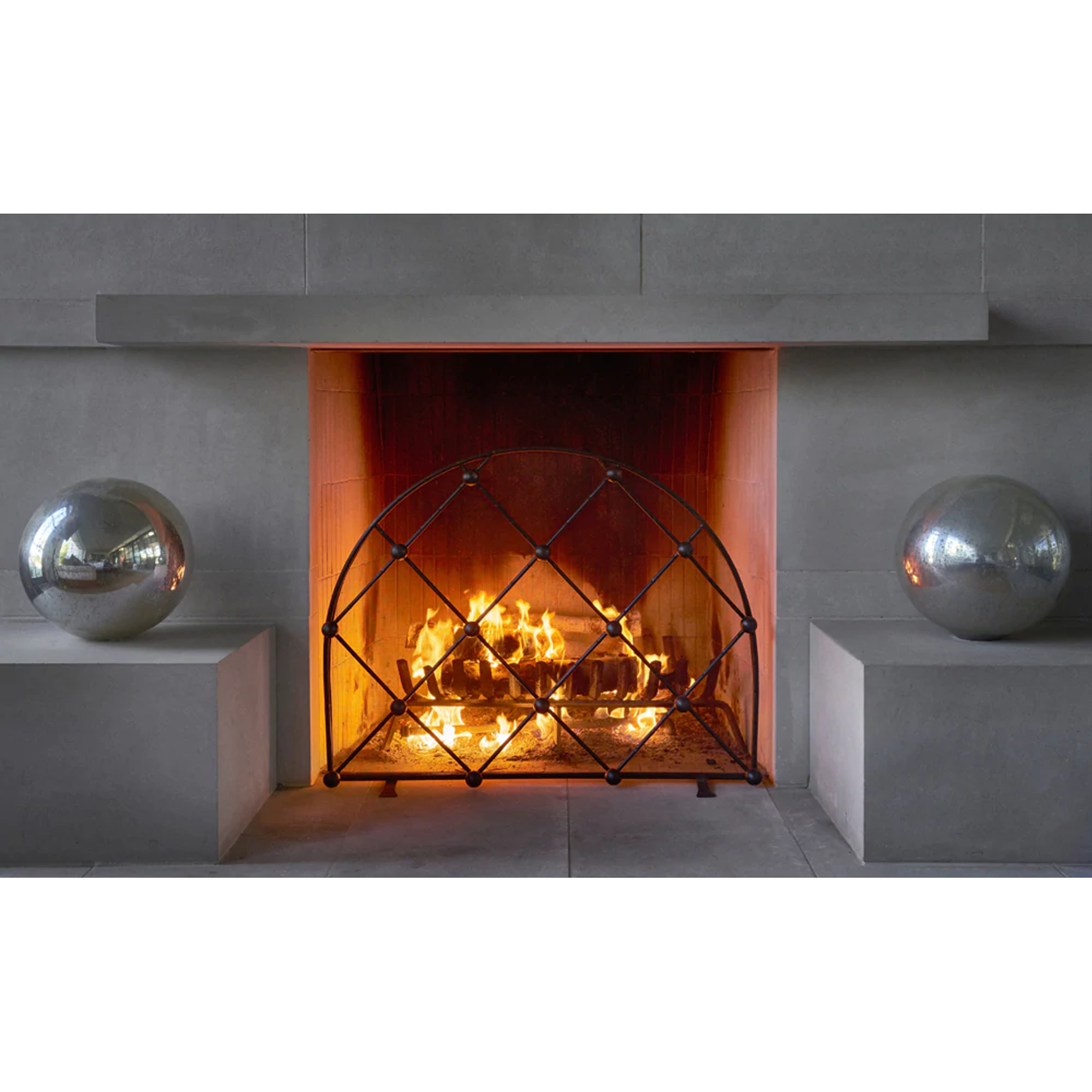A gray wall with a lit chimney, an arched iron fire screen in front and to each side a grey ball.