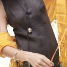 Torso of a woman wearing a black dress and a yellow poncho. She is wearing a necklace with a silver ball and a silver bracelet  with embossed, riveted signature seals.