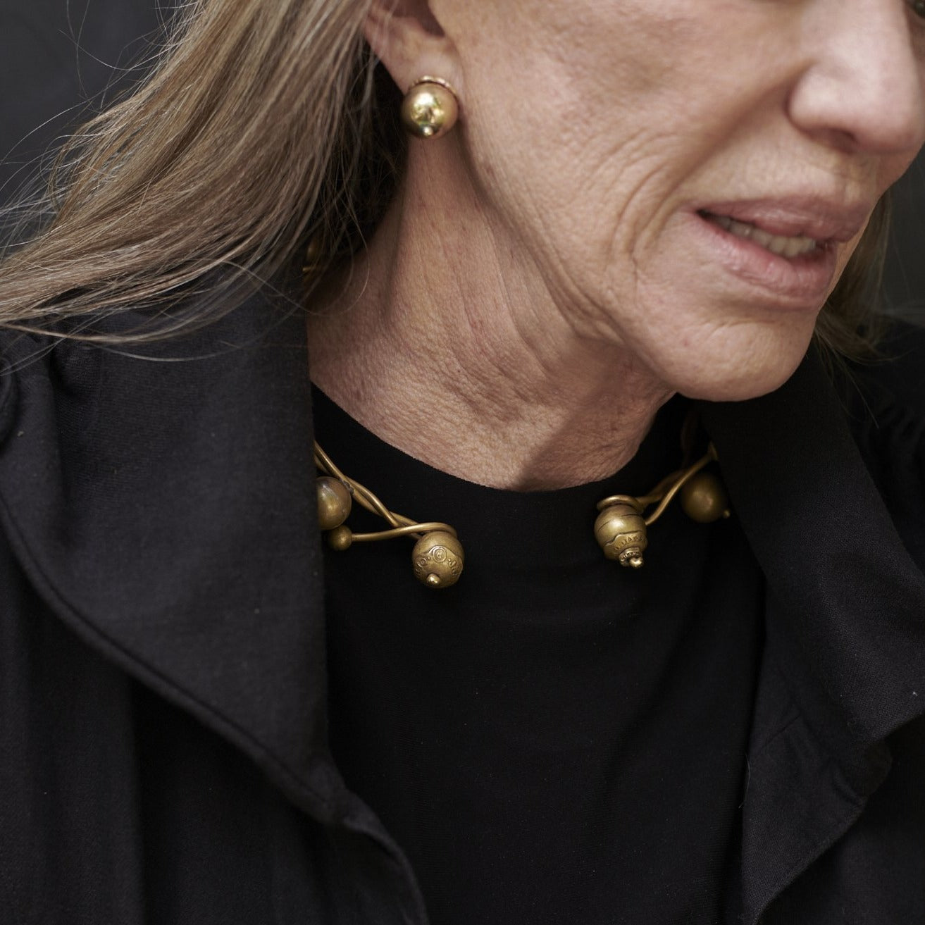 An older woman wearing black clothes and bronze jewelry.