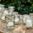 Several glass votives with small lit candles inside each. On top of a light wood.
