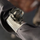 A silver cuff with a dark metal rose in a black sleeves.