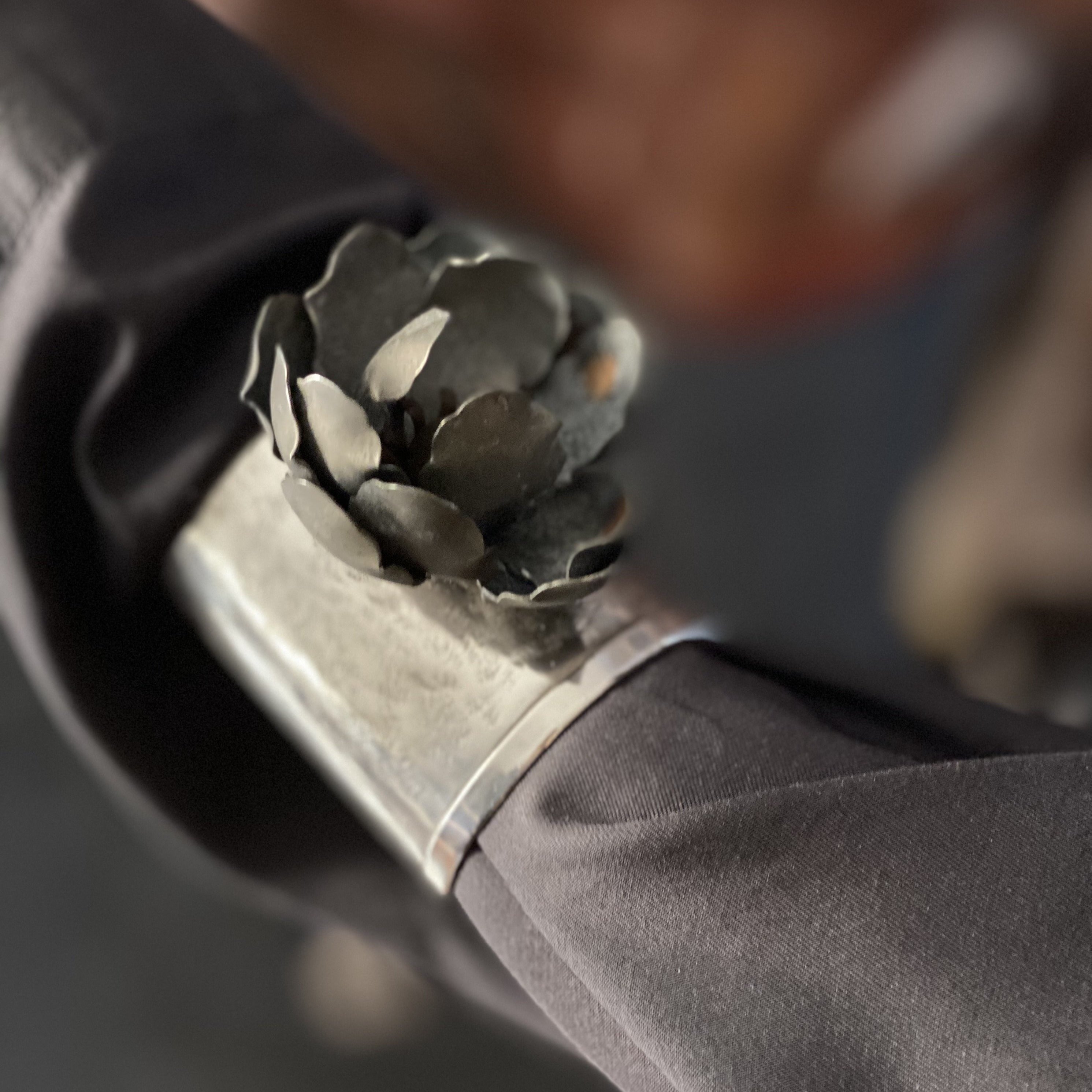 A silver cuff with a dark metal rose in a black sleeves.