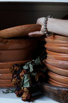 Two towers of several brown plates. A hand holding the upper plate. In the wrist is a silver beads bracelet.  Between the towers is a bouquet of dead roses.