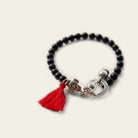 A black bead bracelet with a red string charm and a silver cross charm. Plain background.