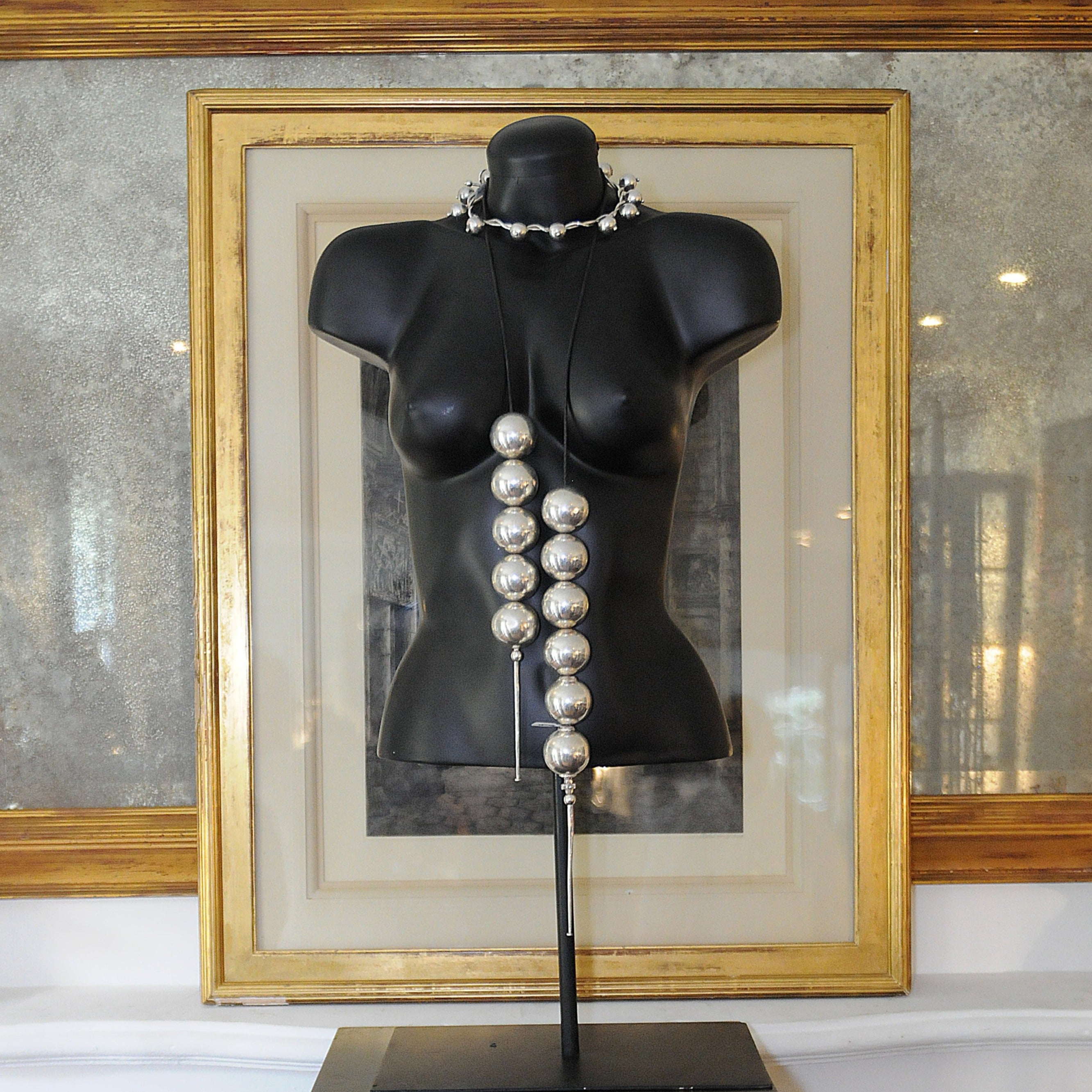A black manikin of a woman's torso with two silver necklaces.
