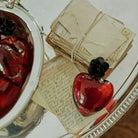Mouth blown puffed red glass heart with a tiny iron rose.  on trop of several handwritten letters. 
