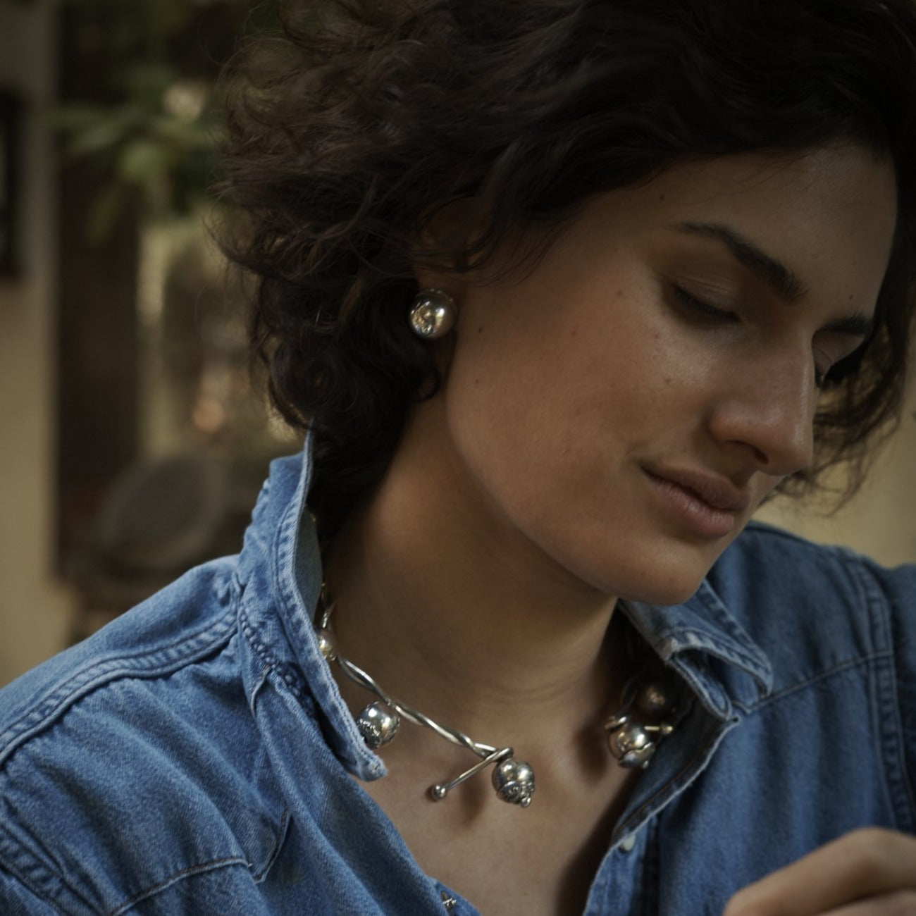 A woman with a denim shirt and silver jewelry.