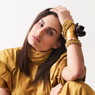 A woman resting her hand in her head. 
 In her wrist are several bronze beads bracelet and a cuff with a dark metal rose.