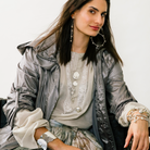 A woman wearing a grey attire. She is wearing several silver jewelry.