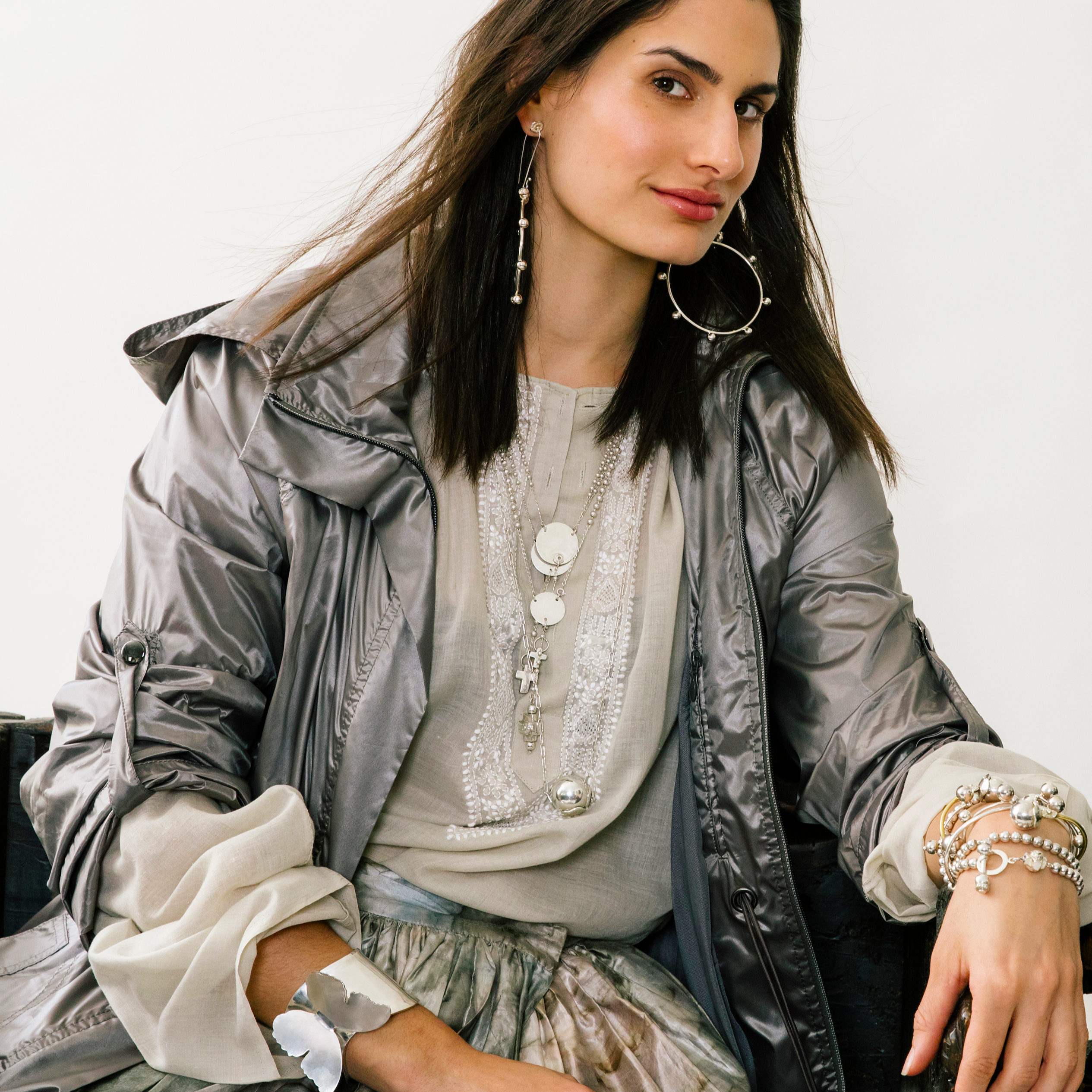 A woman wearing a grey attire. She is wearing several silver jewelry.