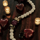 Three mouth blown puffed red glass hearts with a tiny iron rose.  White beads and a red bead in the center and three lit candles.