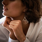 Half of a woman's face in profile, her two hands under her chin. She is wearing a white shirt and in the center in her ear is a silver earring.