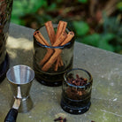 Two glasses with iron coasters. One glass has cinnamon sticks and the other cloves 