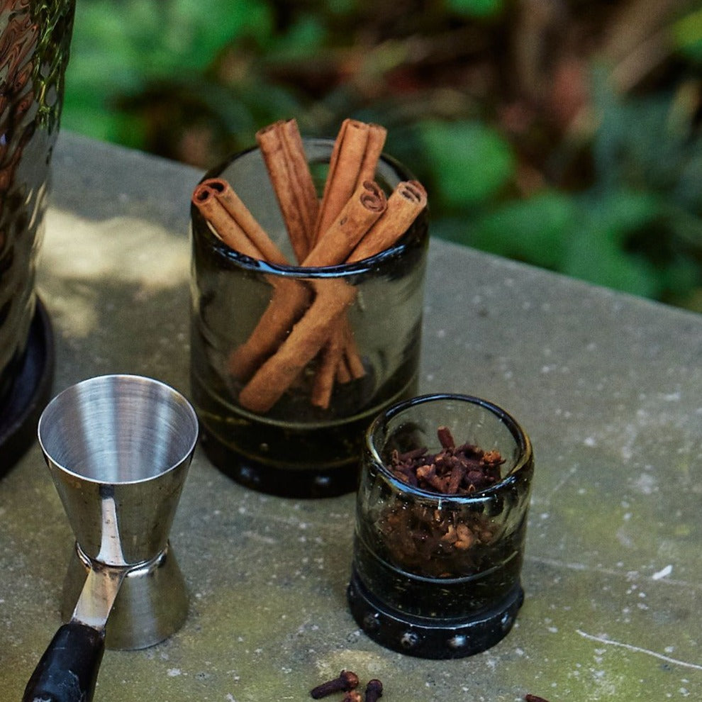 Two glasses with iron coasters. One glass has cinnamon sticks and the other cloves 